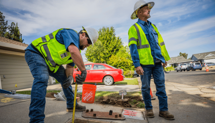 Two water professionals work near an open manhole on a street.